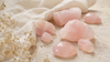 Polerade och råa rosenkvartsstenar i mjuka rosa toner på ljus sten och beige linnetyg.