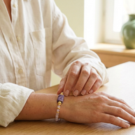 Kvinna som bär ametrin- och charoitarmband vid ett bord