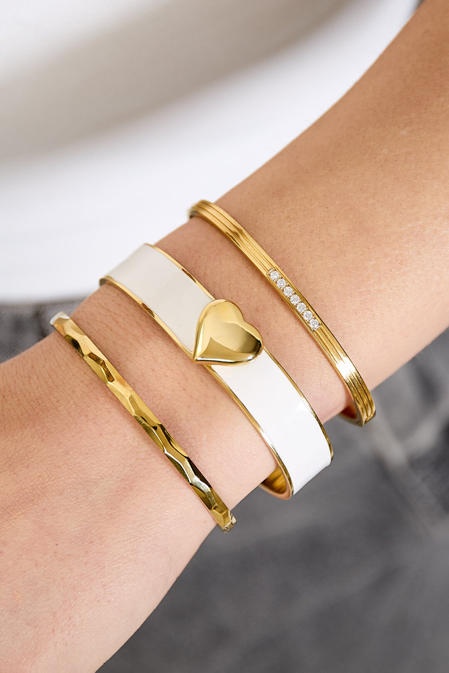 Krämvitt hjärtarmband buret med smala guldfärgade armband
