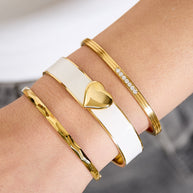 Krämvitt hjärtarmband buret med smala guldfärgade armband