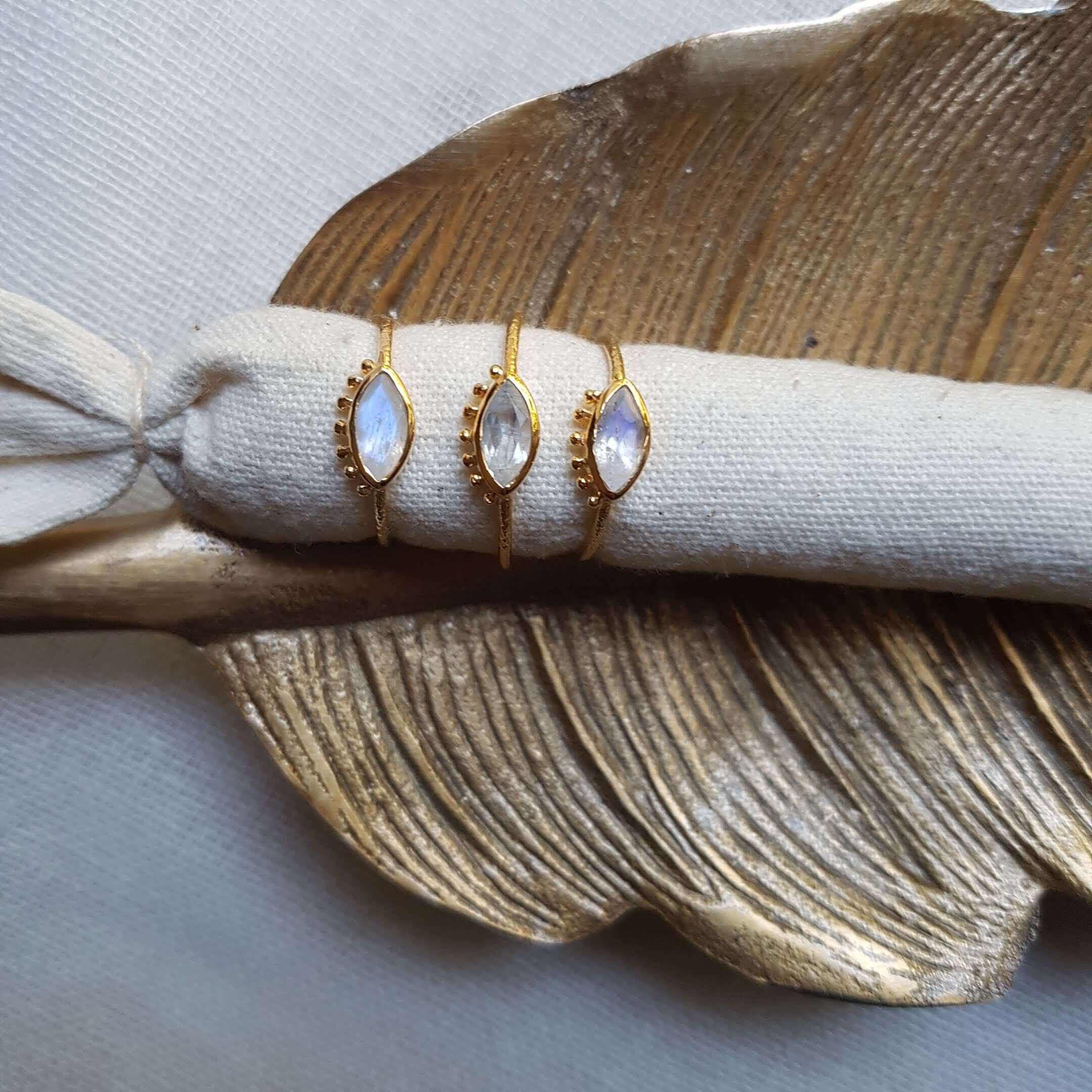 Tre guldfärgade Iris-ringar med ögonmotiv och olika stenar på dekorativt blad