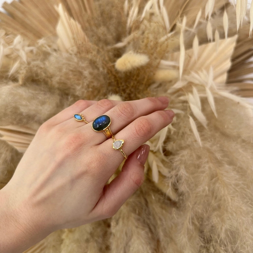 Hand med oval labradoritring tillsammans med flera små stenringar